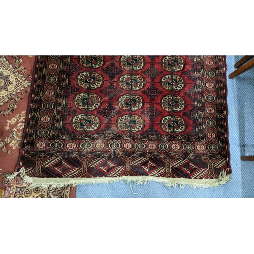 216 - A Pakistani red ground rug having elephant foot motifs and multiguard borders with tasselled ends, 1... 