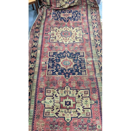 217 - A Turkish hand woven red ground runner having five central motifs and repeating pattern, 322cm x 140... 