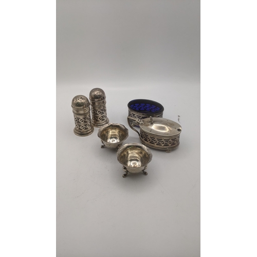 63 - Silver condiments to include a pair of salt and pepper shakers having a pierced design, and blue gla... 