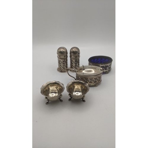 63 - Silver condiments to include a pair of salt and pepper shakers having a pierced design, and blue gla... 