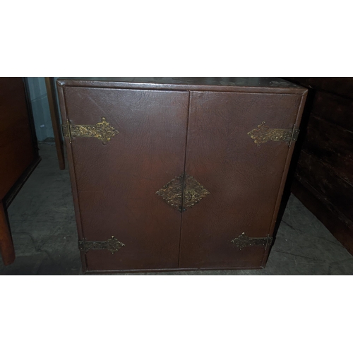 588 - A vintage Korean brown leather two door table top cabinet having cast metal supports and glass shelf... 