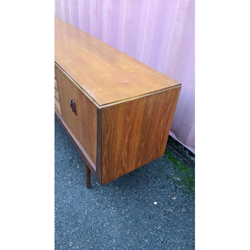 111 - A mid 20th century retro teak sideboard, circa 1960s, having four sliding cupboard doors opening to ... 