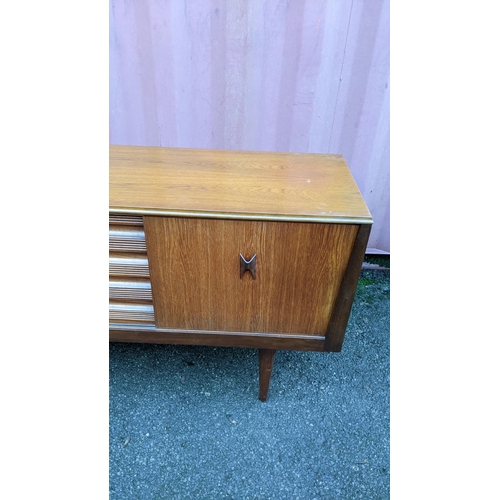 111 - A mid 20th century retro teak sideboard, circa 1960s, having four sliding cupboard doors opening to ... 