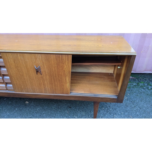 111 - A mid 20th century retro teak sideboard, circa 1960s, having four sliding cupboard doors opening to ... 