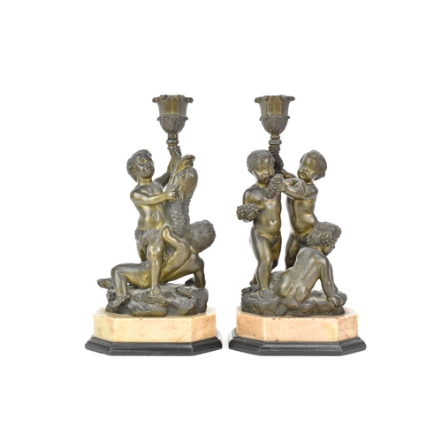 25 - Two 19th century bronze figural candlesticks, each cast with a dolphin and putti holding a cornucopi... 