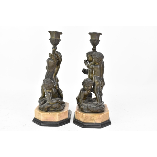 25 - Two 19th century bronze figural candlesticks, each cast with a dolphin and putti holding a cornucopi... 