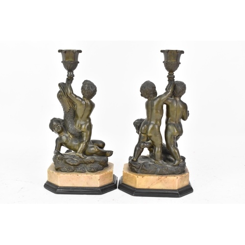 25 - Two 19th century bronze figural candlesticks, each cast with a dolphin and putti holding a cornucopi... 