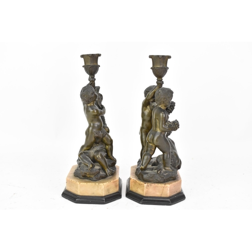 25 - Two 19th century bronze figural candlesticks, each cast with a dolphin and putti holding a cornucopi... 