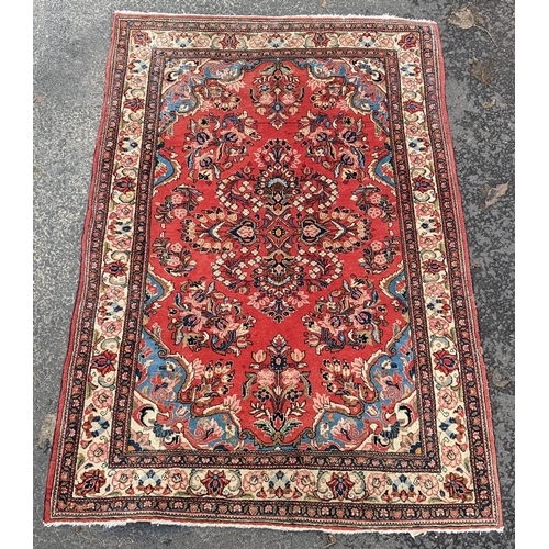 255 - A Persian hand woven rug, having a central motif  surrounded by floral arrangements on a red field a... 