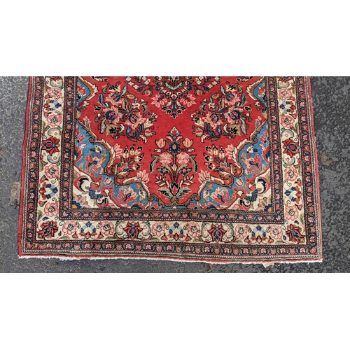 255 - A Persian hand woven rug, having a central motif  surrounded by floral arrangements on a red field a... 