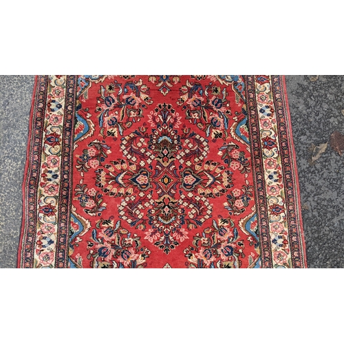 255 - A Persian hand woven rug, having a central motif  surrounded by floral arrangements on a red field a... 