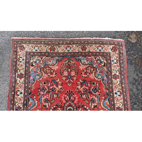 255 - A Persian hand woven rug, having a central motif  surrounded by floral arrangements on a red field a... 