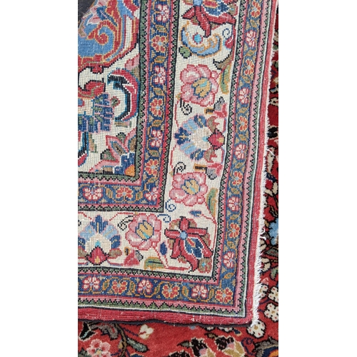 255 - A Persian hand woven rug, having a central motif  surrounded by floral arrangements on a red field a... 