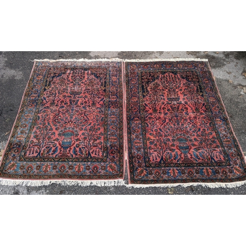 256 - A pair of Persian pictorial hand woven rugs, each on a red ground, the field decorated with an urn, ... 