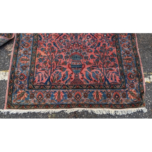 256 - A pair of Persian pictorial hand woven rugs, each on a red ground, the field decorated with an urn, ... 