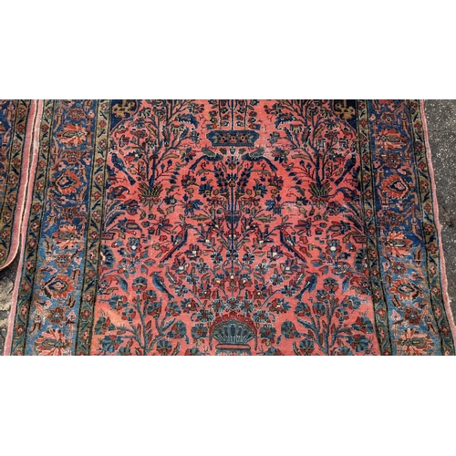 256 - A pair of Persian pictorial hand woven rugs, each on a red ground, the field decorated with an urn, ... 