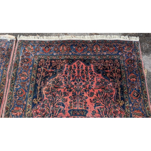 256 - A pair of Persian pictorial hand woven rugs, each on a red ground, the field decorated with an urn, ... 