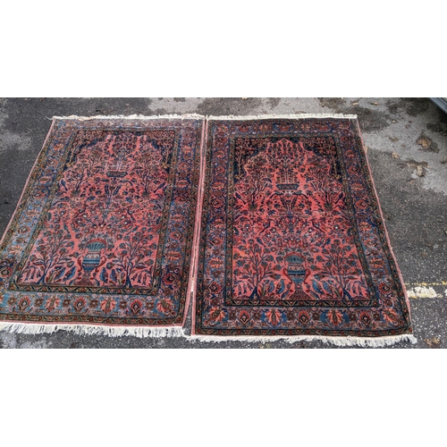 256 - A pair of Persian pictorial hand woven rugs, each on a red ground, the field decorated with an urn, ... 