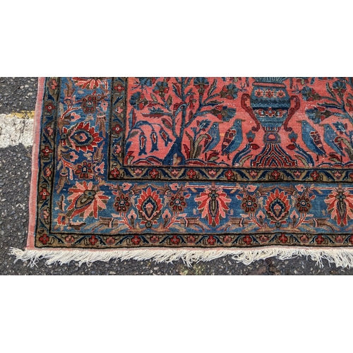 256 - A pair of Persian pictorial hand woven rugs, each on a red ground, the field decorated with an urn, ... 