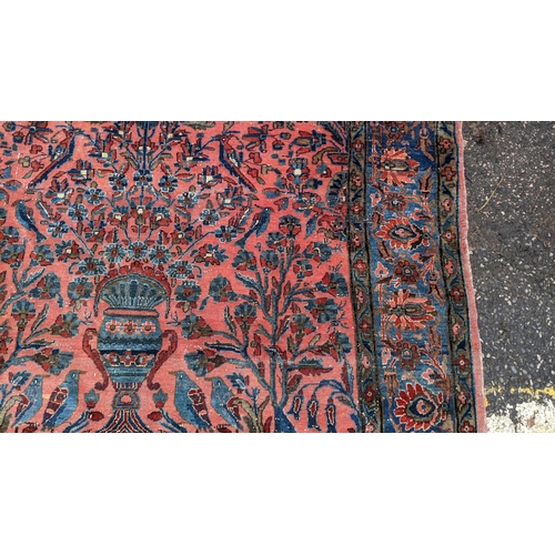 256 - A pair of Persian pictorial hand woven rugs, each on a red ground, the field decorated with an urn, ... 