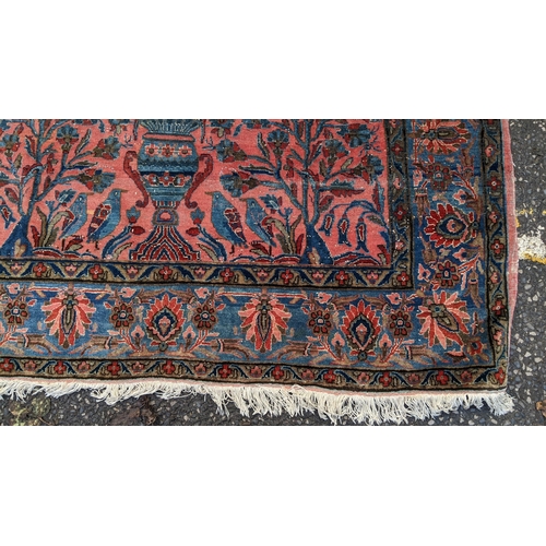 256 - A pair of Persian pictorial hand woven rugs, each on a red ground, the field decorated with an urn, ... 