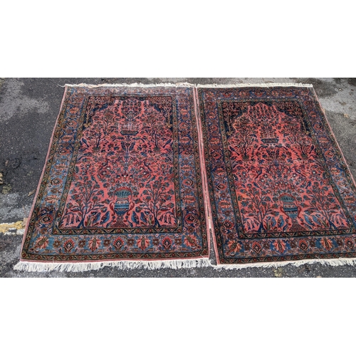 256 - A pair of Persian pictorial hand woven rugs, each on a red ground, the field decorated with an urn, ... 