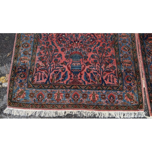 256 - A pair of Persian pictorial hand woven rugs, each on a red ground, the field decorated with an urn, ... 