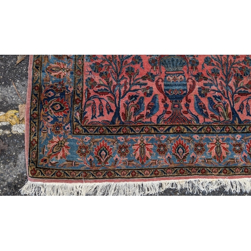 256 - A pair of Persian pictorial hand woven rugs, each on a red ground, the field decorated with an urn, ... 