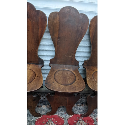 263 - A set of four George II mahogany hall chairs, each of sgabello form with escutcheon shaped backs, ci... 