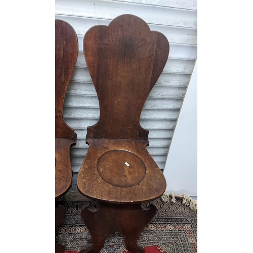 263 - A set of four George II mahogany hall chairs, each of sgabello form with escutcheon shaped backs, ci... 