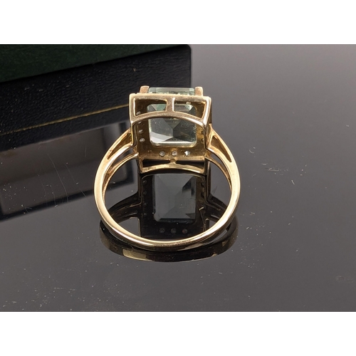 74C - A 9ct gold ring set with an emerald cut aquamarine, 3.6ct, within a border of fourteen diamonds, 3.2... 