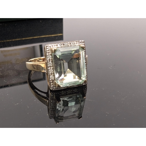 74C - A 9ct gold ring set with an emerald cut aquamarine, 3.6ct, within a border of fourteen diamonds, 3.2... 