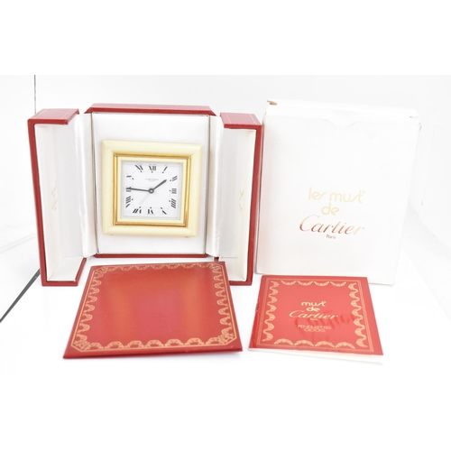 10 - A Cartier travel alarm clock, having a square cream enamel and gilt metal case, the white enamel dia... 