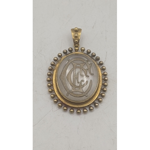 11 - An Victorian possibly rock crystal oval shaped pendant with engraved initials mounted in a yellow go... 