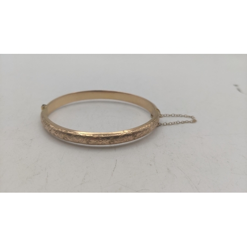 16 - A 9ct yellow gold bangle with engraved floral decoration hinged with safety chain 7g
Location:CAB4
I... 