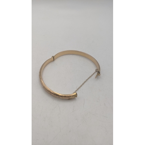 16 - A 9ct yellow gold bangle with engraved floral decoration hinged with safety chain 7g
Location:CAB4
I... 