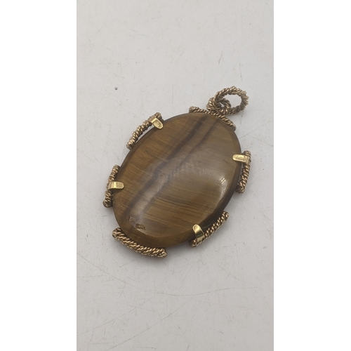 58 - An oval shaped tiger eye pendant mounted in a 9ct yellow gold rope twist style frame, total weight 2... 