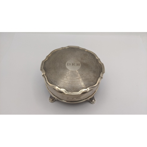 74 - An silver dressing table ring box in circular form on four feet having an engine turned lid engraved... 