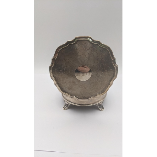 74 - An silver dressing table ring box in circular form on four feet having an engine turned lid engraved... 