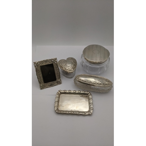 76 - Silver dressing table collectables to include an heart shaped glass and silver lidded pot having flo... 