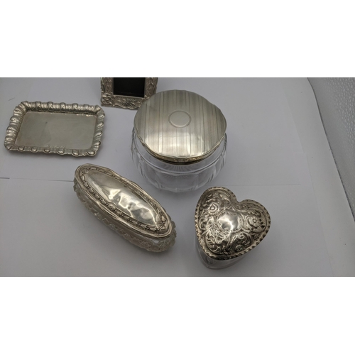 76 - Silver dressing table collectables to include an heart shaped glass and silver lidded pot having flo... 