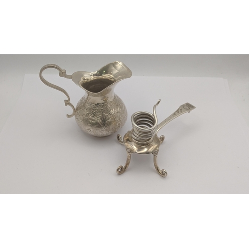 77 - A white metal cream jug decorated with floral and figural decoration, along with a white metal usual... 