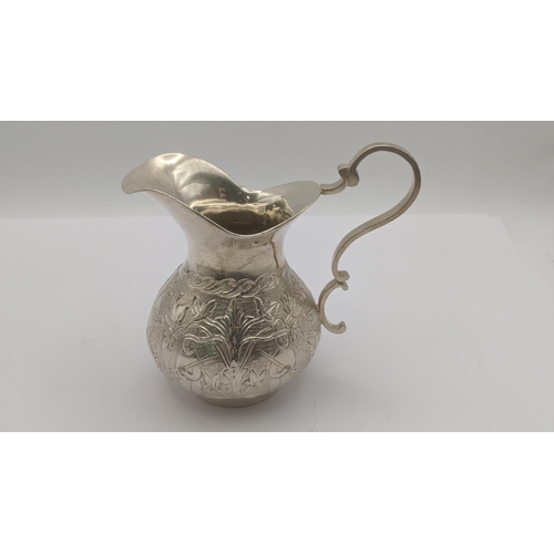 77 - A white metal cream jug decorated with floral and figural decoration, along with a white metal usual... 