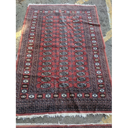 311 - TWo hand woven red ground Pakistan Bukhara rugs, three  vertical rows of 14 elephant gulls, alternat... 