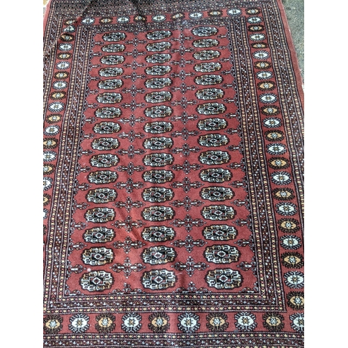 311 - TWo hand woven red ground Pakistan Bukhara rugs, three  vertical rows of 14 elephant gulls, alternat... 