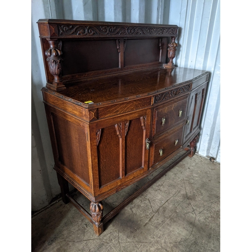 345 - An early 20th century oak highboard with a panelled backpiece supported by a pair of ornately decora... 