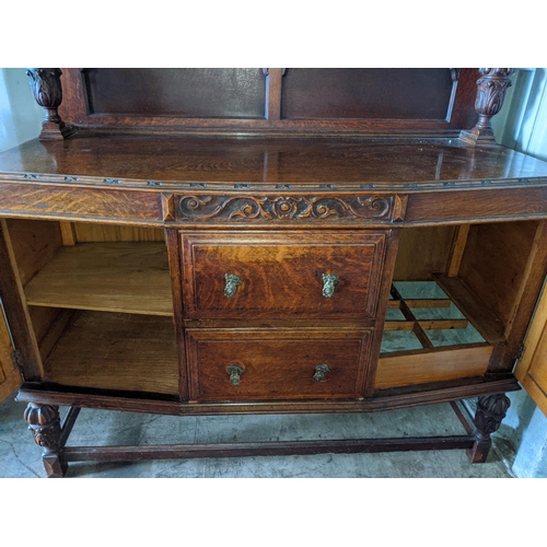 345 - An early 20th century oak highboard with a panelled backpiece supported by a pair of ornately decora... 