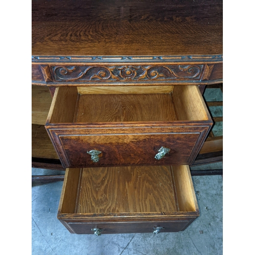 345 - An early 20th century oak highboard with a panelled backpiece supported by a pair of ornately decora... 