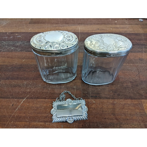 64 - Two silver topped dressing table jars with engraved ornament and a plain decanter label
Location:6.4... 