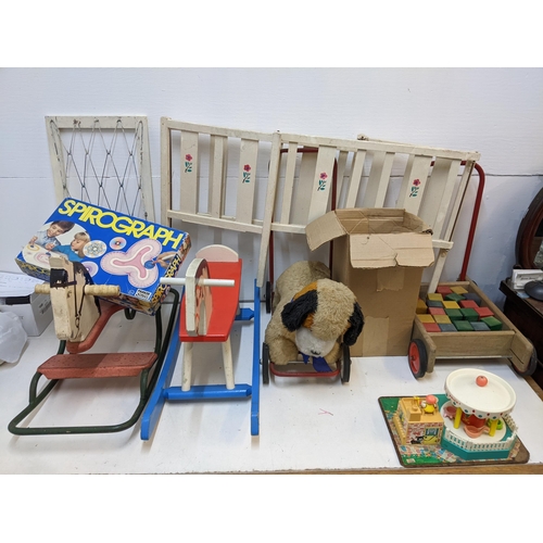 207 - A collection of vintage toys to include two rocking horses, a Fisher Price roundabout, a dolls cot, ... 